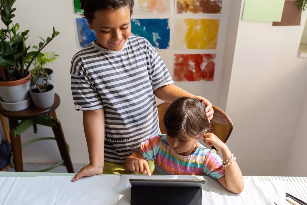 Two young boys at a table together looking at a tablet screen
